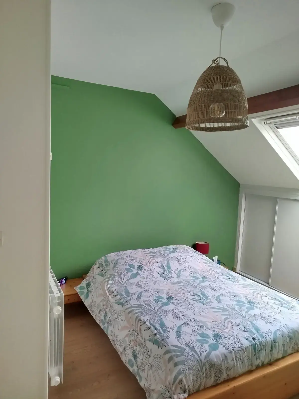Chambre mansardée repeinte en vert, poutre apparente et fenêtre de toit