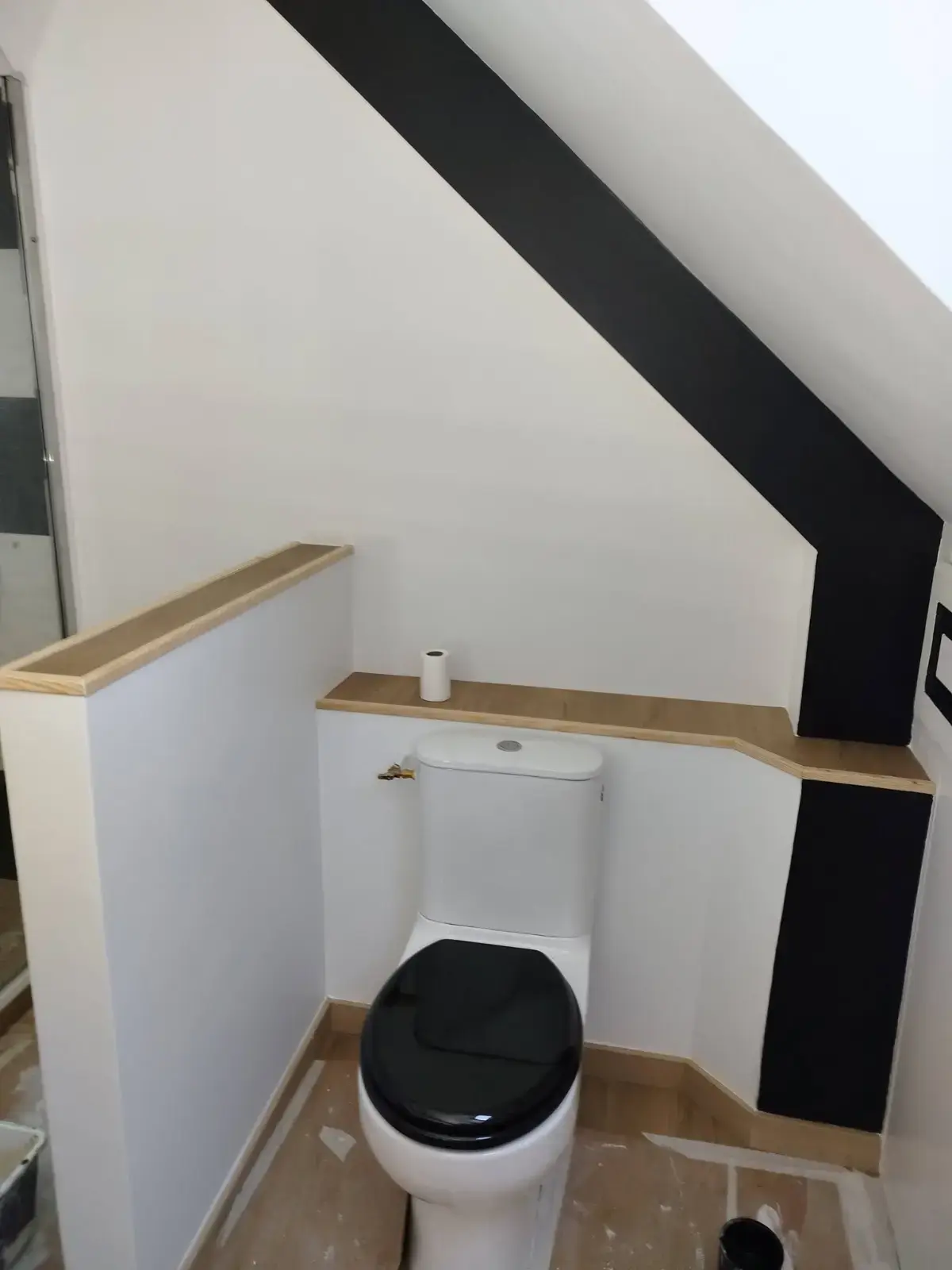 WC sous combles : murs blancs et bande noire soulignant la charpente
